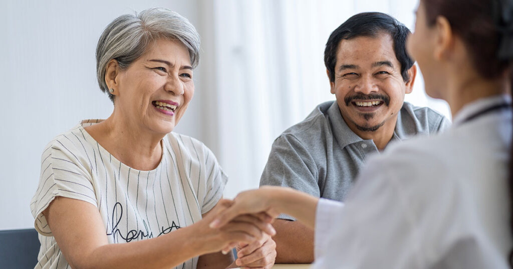 Retired couple sitting down and shaking hands with advisor.