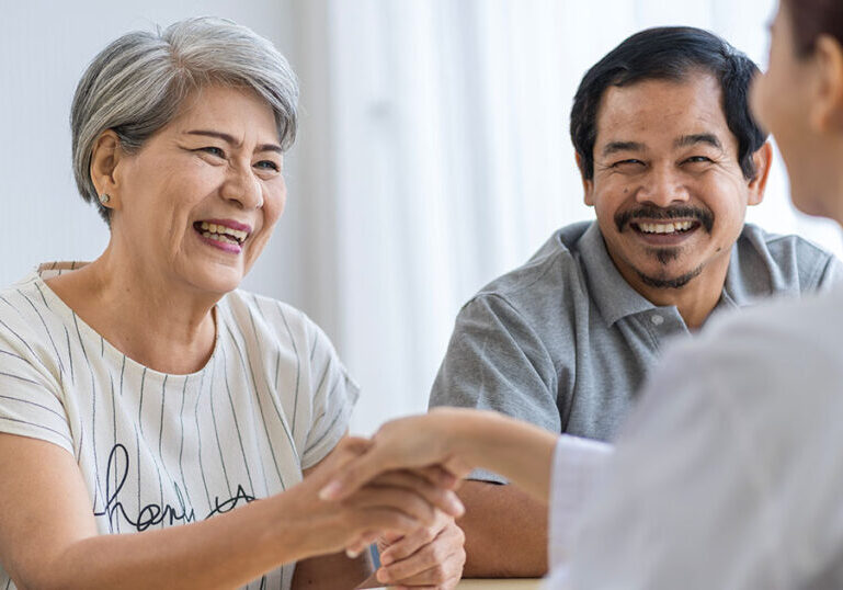 Retired couple sitting down and shaking hands with advisor.