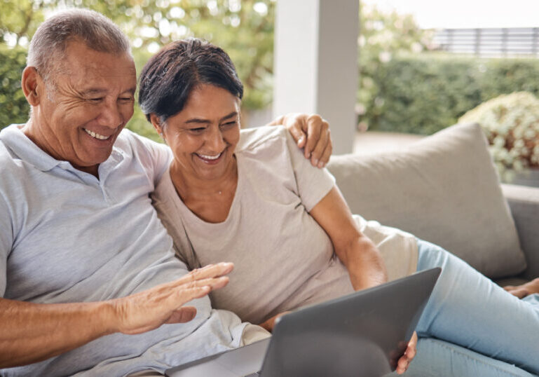 Older U.S. expat couple relaxing on an outdoor sofa, looking at a laptop together as they review their finances and plan for common financial obstacles while living abroad