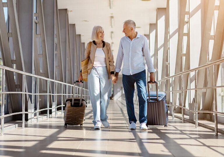 A retired couple walking together with luggage through an airport terminal or walkway, representing confident retirement travel planning.