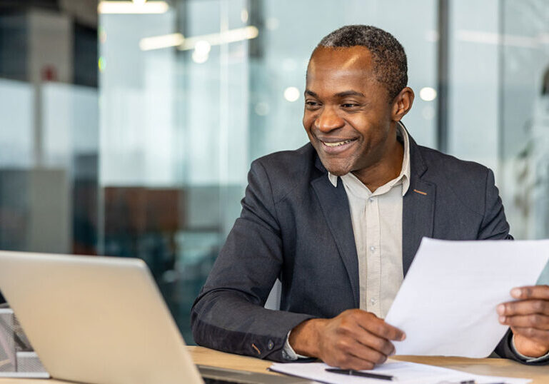 Corporate executive smiling while reviewing financial documents at a laptop, symbolizing comprehensive executive financial planning that aligns compensation, investments, taxes and cash flow with long‑term goals